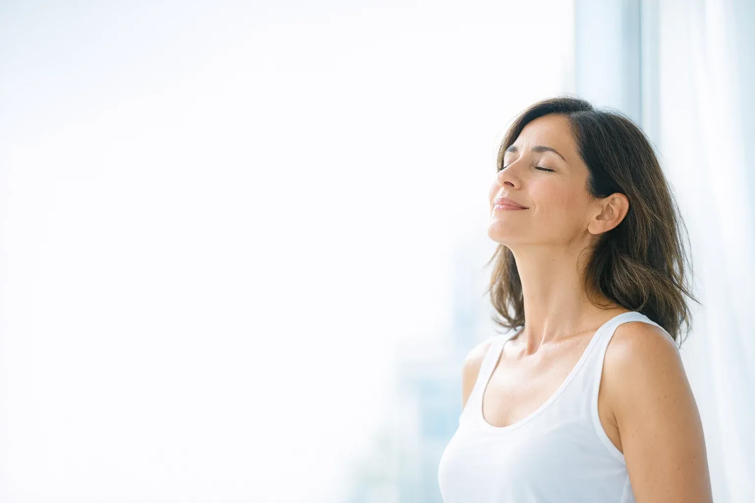Mujer respirando en calma junto a la ventana: bienestar y acompañamiento